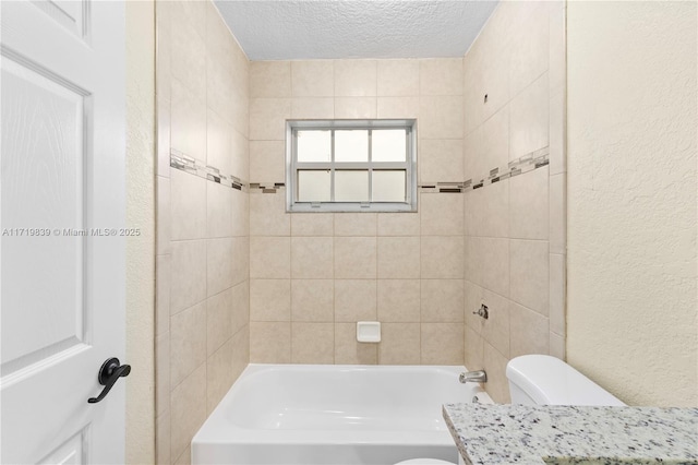 bathroom featuring a textured ceiling, toilet, and tiled shower / bath combo