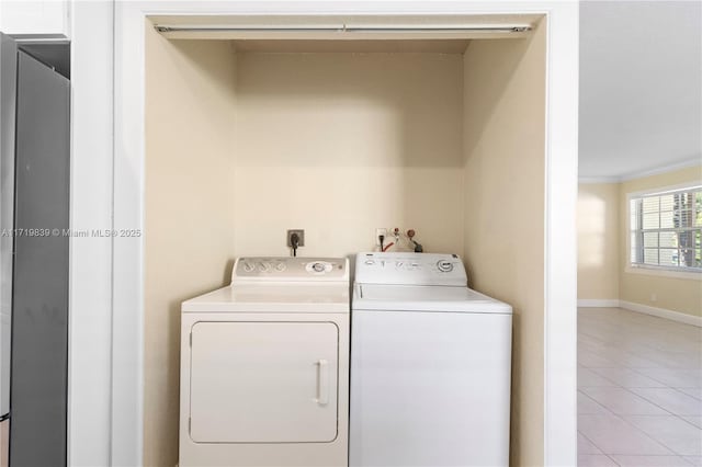 clothes washing area featuring light tile patterned floors, crown molding, and washing machine and clothes dryer