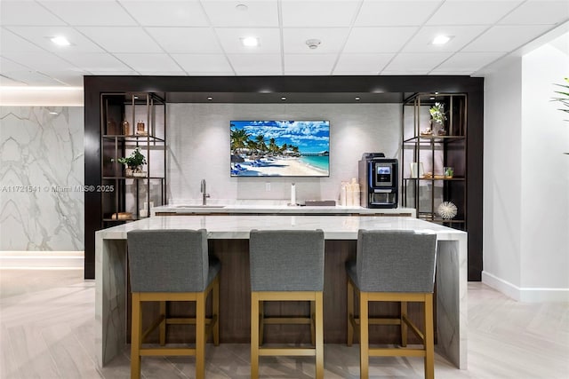 bar featuring light stone countertops, sink, light parquet floors, and a drop ceiling