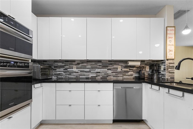 kitchen with sink, hanging light fixtures, stainless steel appliances, tasteful backsplash, and white cabinets