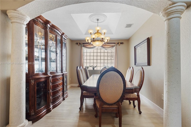 dining room with a chandelier, decorative columns, a raised ceiling, and light hardwood / wood-style flooring