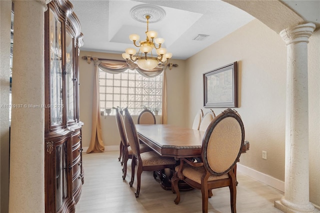 dining space featuring a notable chandelier, a raised ceiling, and decorative columns