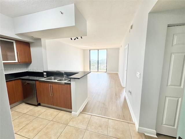 kitchen featuring open floor plan, a peninsula, stainless steel dishwasher, brown cabinetry, and a sink