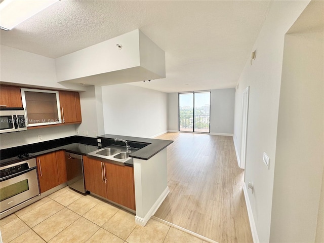 kitchen featuring brown cabinets, a sink, dark countertops, appliances with stainless steel finishes, and a peninsula