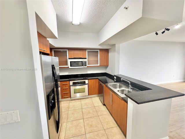 kitchen featuring a peninsula, a sink, appliances with stainless steel finishes, dark countertops, and brown cabinets