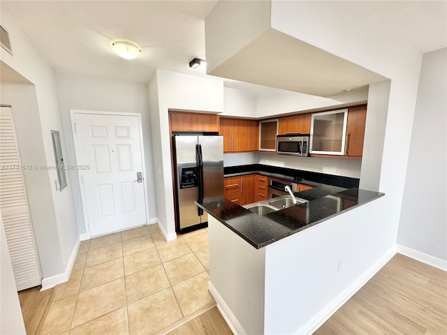 kitchen with glass insert cabinets, brown cabinets, appliances with stainless steel finishes, a peninsula, and a sink