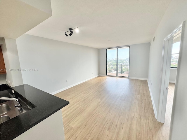 unfurnished living room with visible vents, baseboards, expansive windows, light wood-style floors, and a sink