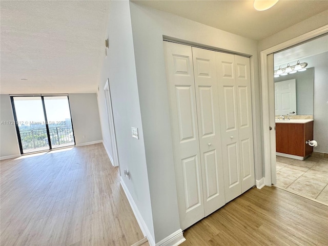 hallway featuring a sink, baseboards, light wood finished floors, and expansive windows