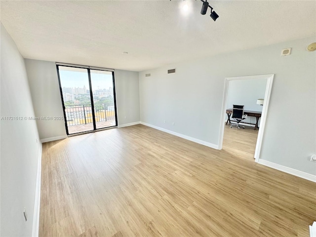 spare room with baseboards, visible vents, floor to ceiling windows, a textured ceiling, and light wood-type flooring