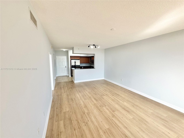 unfurnished living room featuring baseboards, visible vents, light wood finished floors, and a textured ceiling