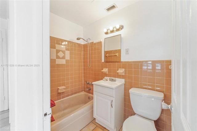 full bathroom featuring tiled shower / bath combo, tile patterned flooring, toilet, vanity, and tile walls