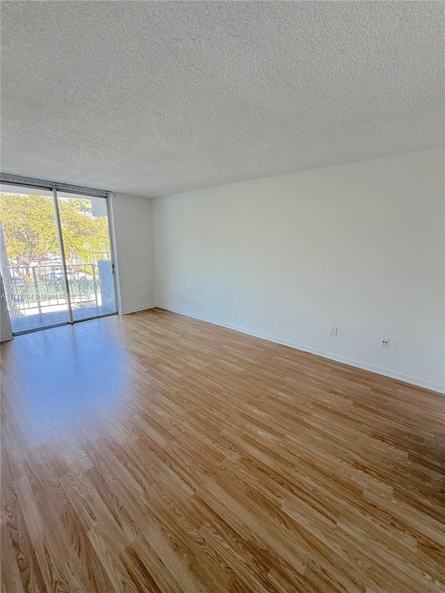 empty room featuring light wood-style floors, expansive windows, baseboards, and a textured ceiling