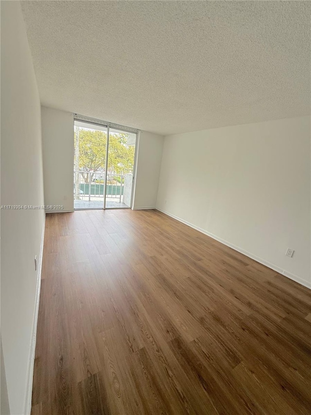 empty room with a textured ceiling, baseboards, wood finished floors, and floor to ceiling windows