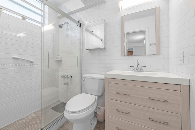 bathroom featuring a shower with door, vanity, tile walls, and toilet