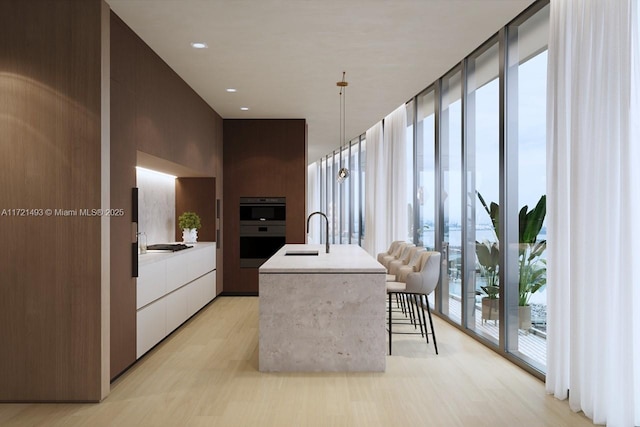 kitchen featuring pendant lighting, expansive windows, sink, an island with sink, and double oven