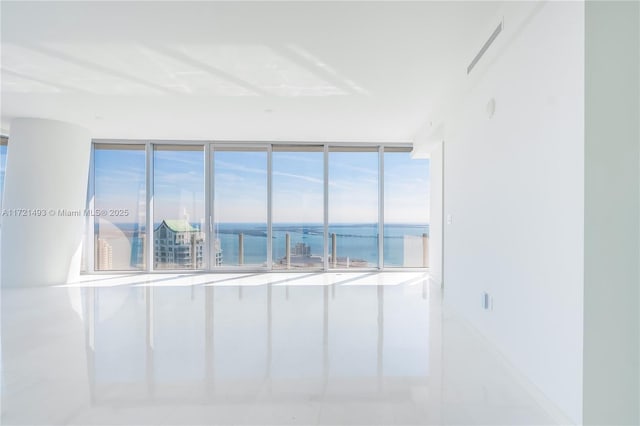 unfurnished room featuring tile patterned floors, a water view, and a wall of windows