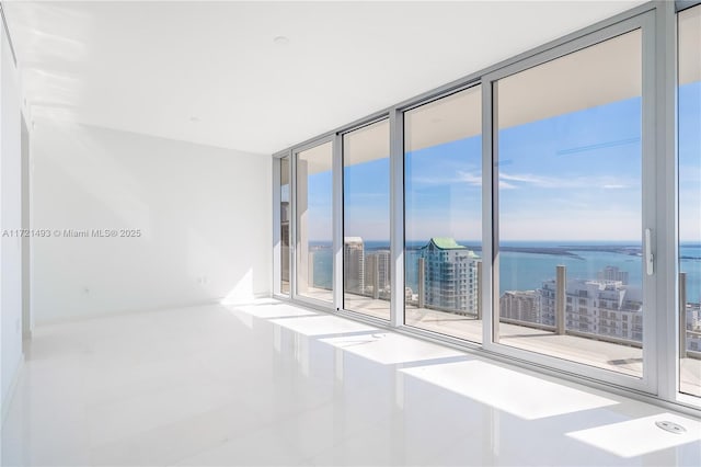 empty room with tile patterned floors, a healthy amount of sunlight, a water view, and a wall of windows