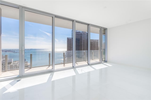 tiled empty room featuring floor to ceiling windows, a water view, and a healthy amount of sunlight