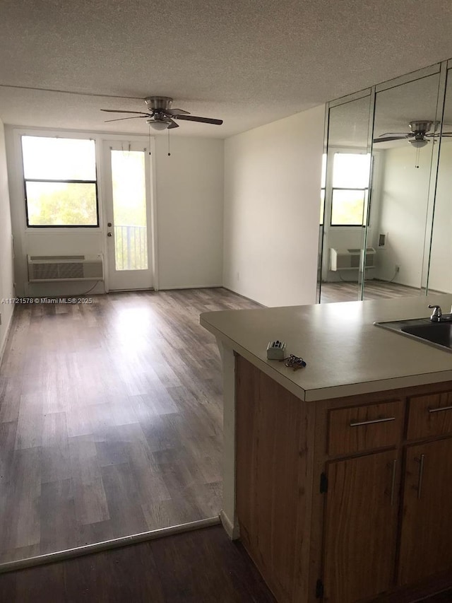 kitchen featuring ceiling fan, sink, a wall unit AC, wood-type flooring, and a textured ceiling