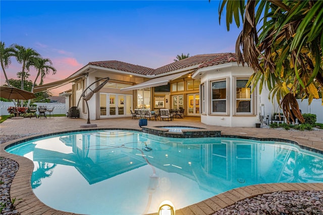 pool at dusk featuring an in ground hot tub, french doors, and a patio area