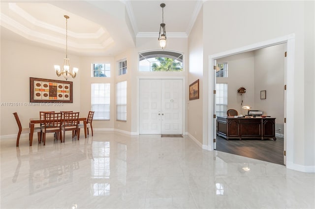 foyer with a raised ceiling, a towering ceiling, a chandelier, and ornamental molding