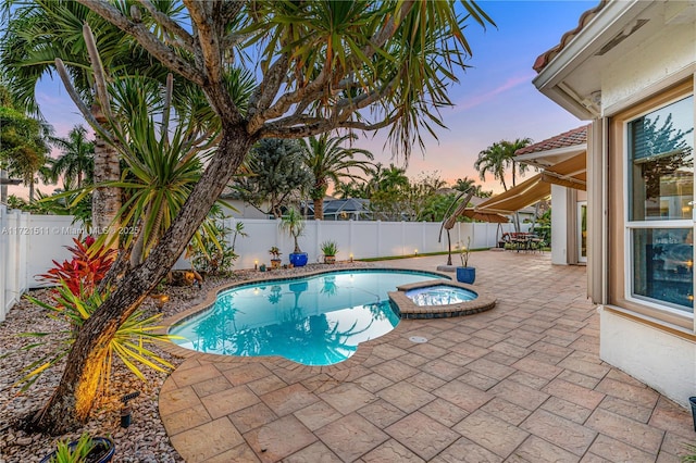 pool at dusk featuring an in ground hot tub and a patio