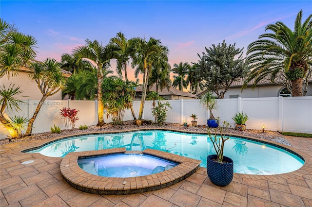 pool at dusk featuring a patio area and an in ground hot tub