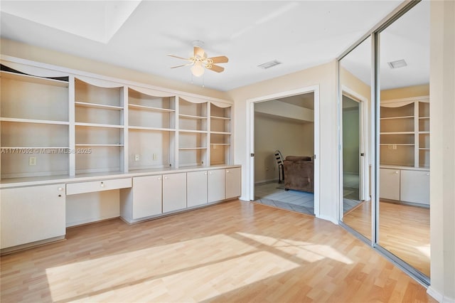 unfurnished office featuring ceiling fan, built in desk, and light wood-type flooring