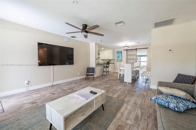 living room with ceiling fan, light hardwood / wood-style floors, and a barn door