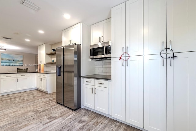 kitchen featuring white cabinets, light wood-type flooring, stainless steel appliances, and backsplash