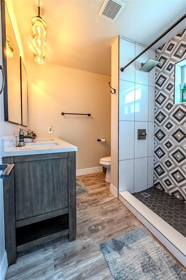 bathroom featuring hardwood / wood-style flooring, vanity, a tile shower, and toilet