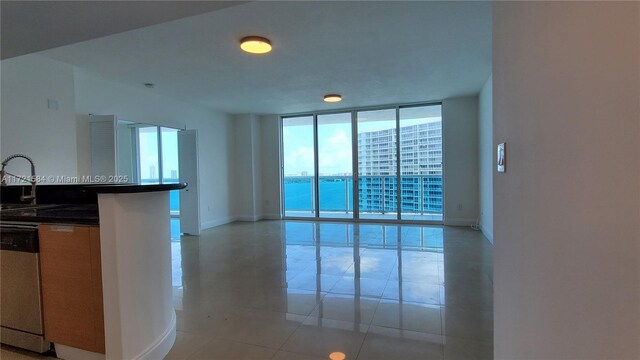 kitchen with floor to ceiling windows, sink, a water view, dishwasher, and light tile patterned flooring