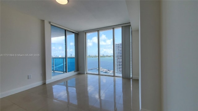 empty room with floor to ceiling windows, a water view, and light tile patterned floors