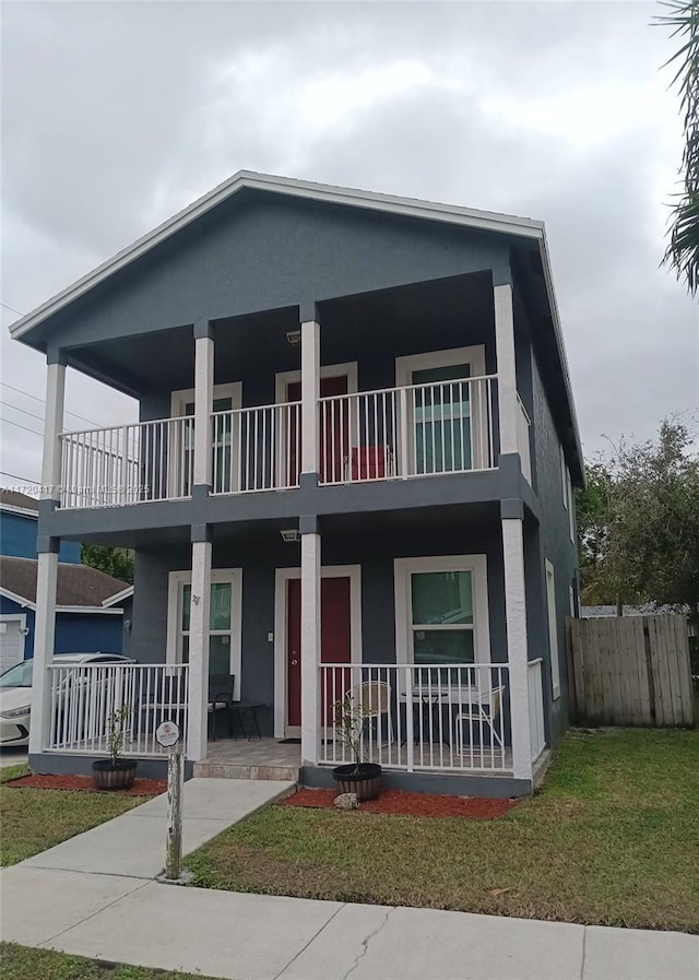 view of front facade featuring covered porch, a garage, a balcony, and a front lawn