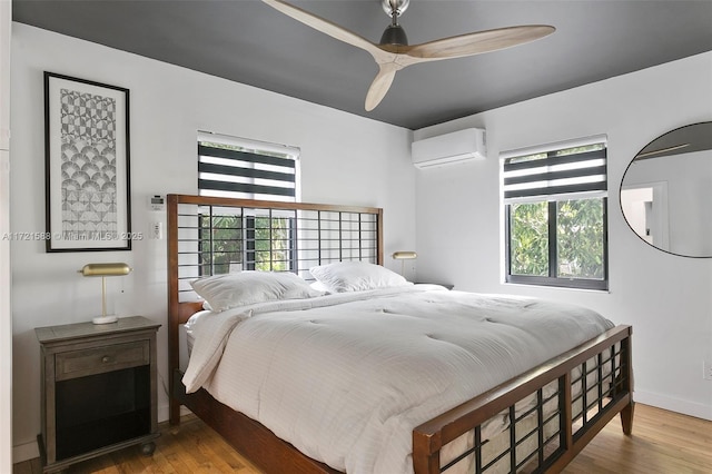 bedroom featuring multiple windows, ceiling fan, a wall mounted air conditioner, and hardwood / wood-style flooring