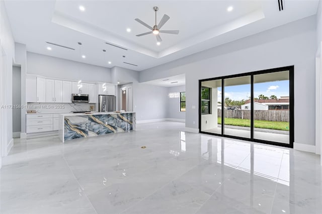 unfurnished living room featuring a high ceiling, a tray ceiling, and ceiling fan