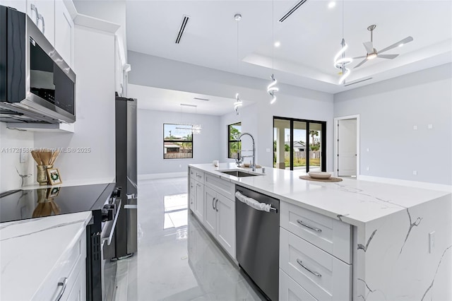 kitchen with light stone countertops, appliances with stainless steel finishes, ceiling fan, sink, and white cabinets