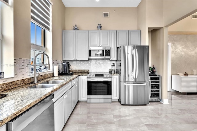 kitchen featuring appliances with stainless steel finishes, a towering ceiling, beverage cooler, sink, and stone counters