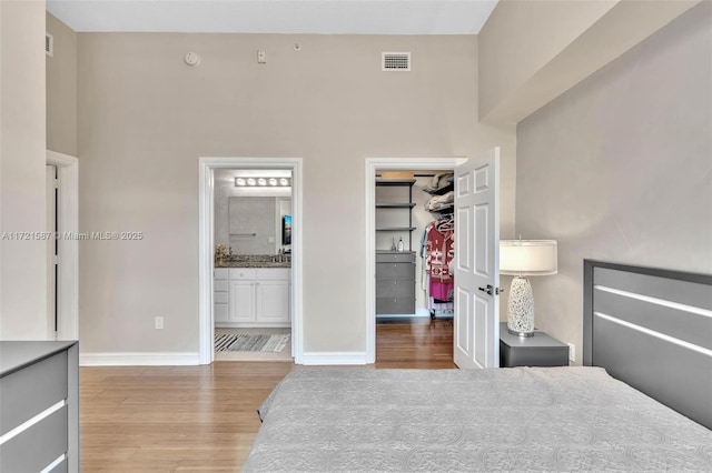 bedroom featuring connected bathroom, a spacious closet, a high ceiling, hardwood / wood-style floors, and a closet