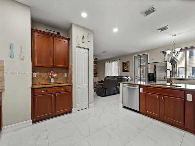 kitchen with pendant lighting, ceiling fan with notable chandelier, sink, appliances with stainless steel finishes, and tasteful backsplash