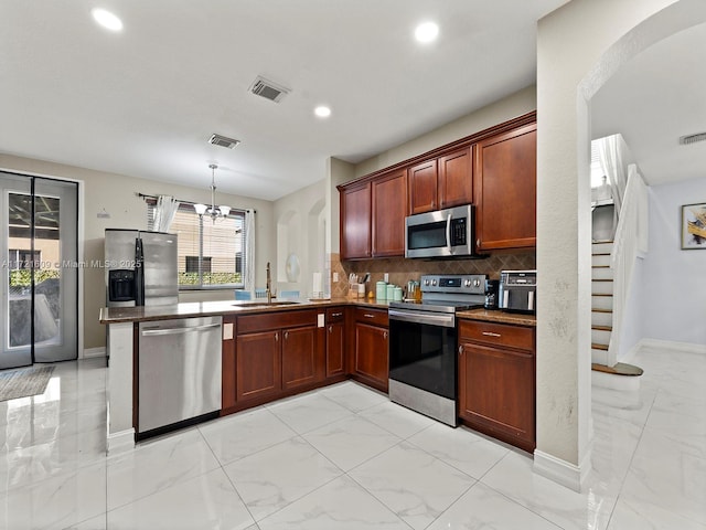 kitchen featuring kitchen peninsula, tasteful backsplash, stainless steel appliances, sink, and hanging light fixtures