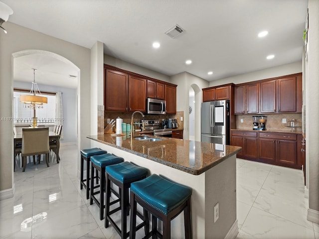 kitchen featuring kitchen peninsula, appliances with stainless steel finishes, a kitchen bar, decorative backsplash, and sink