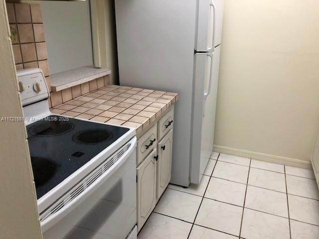 kitchen featuring tile countertops, white cabinets, white appliances, and light tile patterned floors