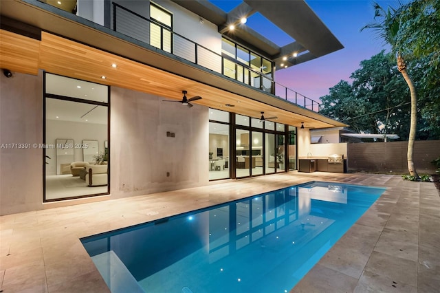 pool at dusk featuring a patio, an outdoor kitchen, fence, a ceiling fan, and a fenced in pool