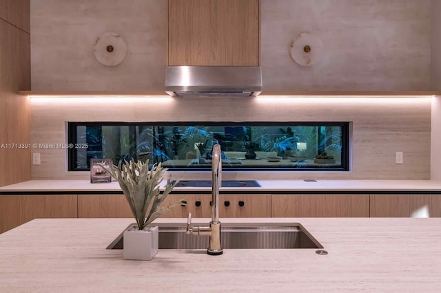 kitchen with light countertops, a sink, under cabinet range hood, and modern cabinets