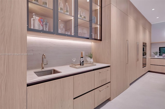 kitchen featuring tasteful backsplash, light countertops, glass insert cabinets, a sink, and modern cabinets