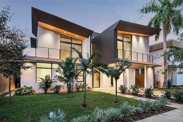 contemporary house featuring a front lawn, a balcony, and stucco siding