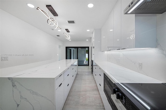 kitchen with range, hanging light fixtures, white cabinets, light stone countertops, and wall chimney range hood