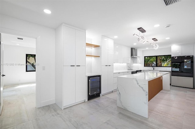 kitchen featuring white cabinetry, wall chimney exhaust hood, black fridge, and hanging light fixtures