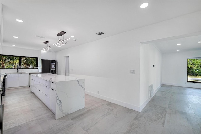 kitchen featuring a spacious island, sink, white cabinetry, black fridge, and hanging light fixtures